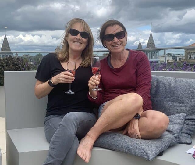 Jude and Ruby Co-founders of Two passports One Planet Travel Blog sitting on a balcony drinking champagne with city skyline behind.