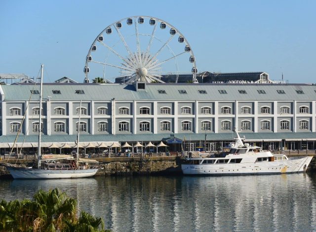 Cape Town Waterfront Hotel and Ferris Wheel behind. Boats moored at the dock in front of the hotel.