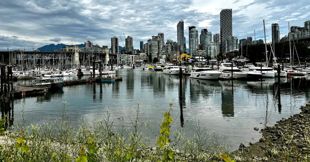 A view of Vancouver, Canada city from boat harbour. Multi story skyline and behind are mountain peaks.  Small boats anchored in the harbour.