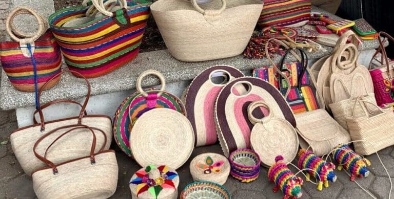 Rows of straw bags and purses lined up on on street sidewalk.