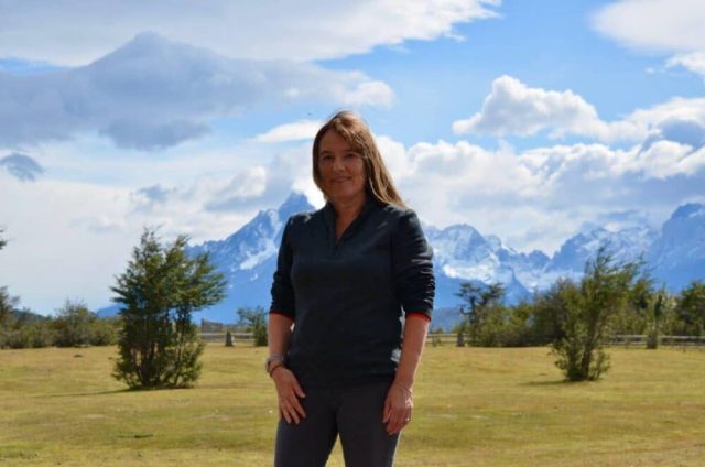 Travel blogger Jude is standing in a grassy field and behind her are snow peaked mountains of Patagonia, Chile.