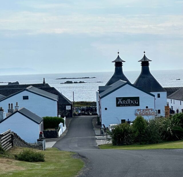 Whitewashed buildings next to the sea are where Ardberg whisky is distilled. Malt towers are visible.