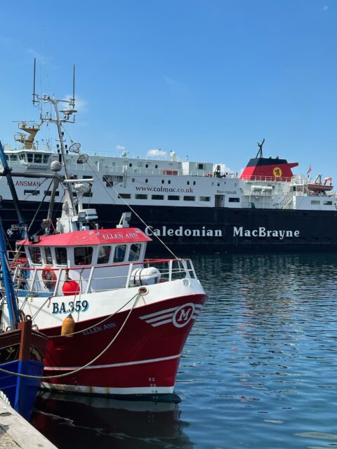 A fishing boat is harbored in Oban, Scotland. Behind it is a larger ferry heading to the Western Isles.