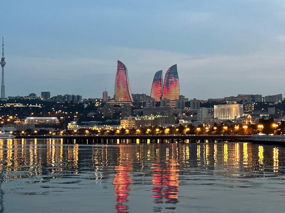 Baku Azerbaijan city skyline with three flame towers showcasing new architecture in the capital city. Lights reflect red and yellow on the Caspian Sea.