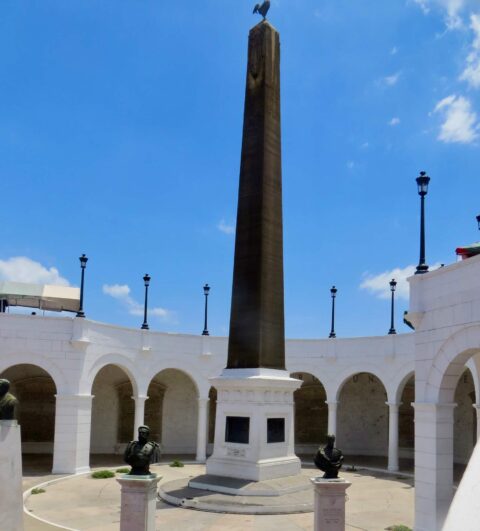 Plaza in the center of a square with a building and white arches around it.