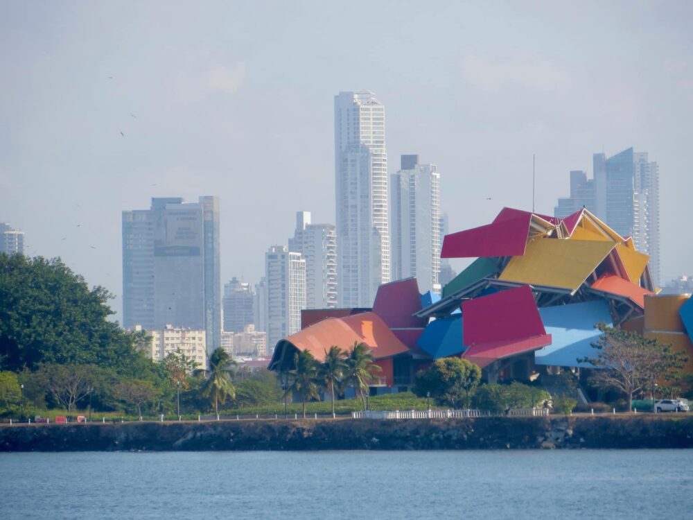 Panama City skyline shows glass skyscrapers in the background. Closer to the water is a red, yellow and blue abstract designed building.