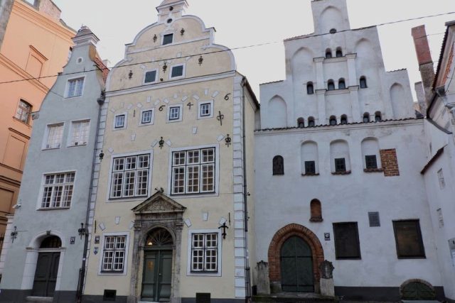 3 homes in Riga, Latvia each built in a different century. One is white, one yellow and one blue.