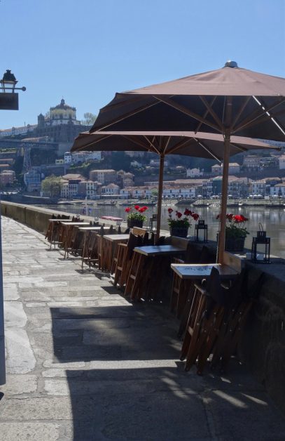 A restaurant has a line of tables along a river all with views over the Douro River and city.