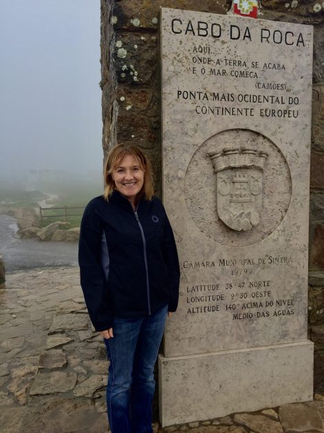 A person is standing at Cabo Da Roca. A stone plague explains the longitude and latitude of this western point of continental Europe.