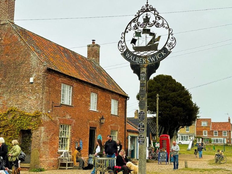Walberwick Village Sign and red brick building with people and dogs walking around.