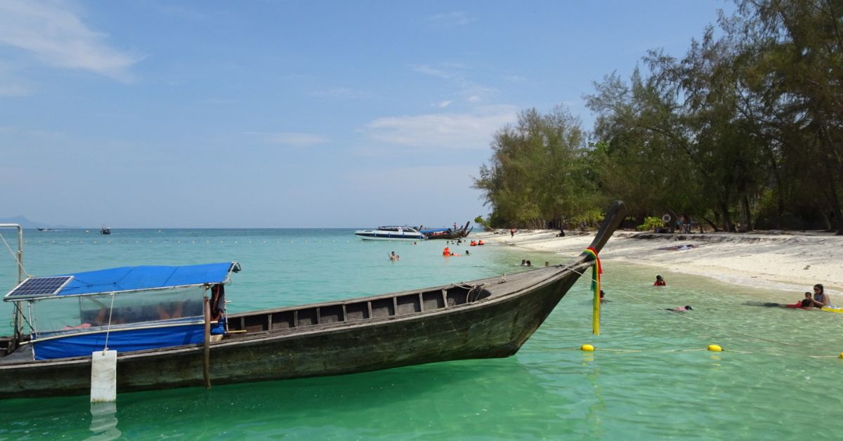 Long boat in the water by the shore with turquoise waters and blue skies. A few people in the water